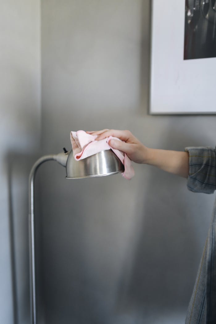 A hand cleaning a metallic lamp with a pink cloth indoors, focusing on housekeeping.